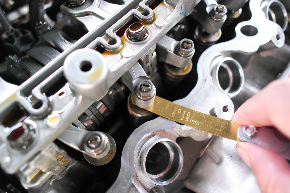 Closeup of engine valve adjustment with feeler gauge, mechanic working and car repair, automotive maintenance in auto service garage.