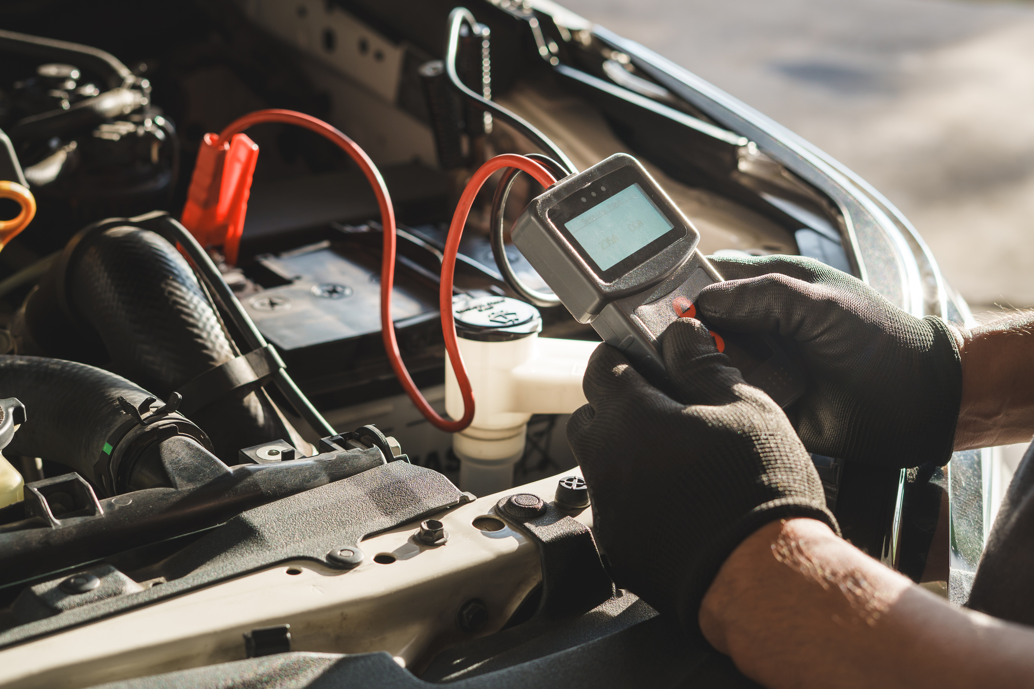 A mechanic connecting an electrical testing device under the hood of a car