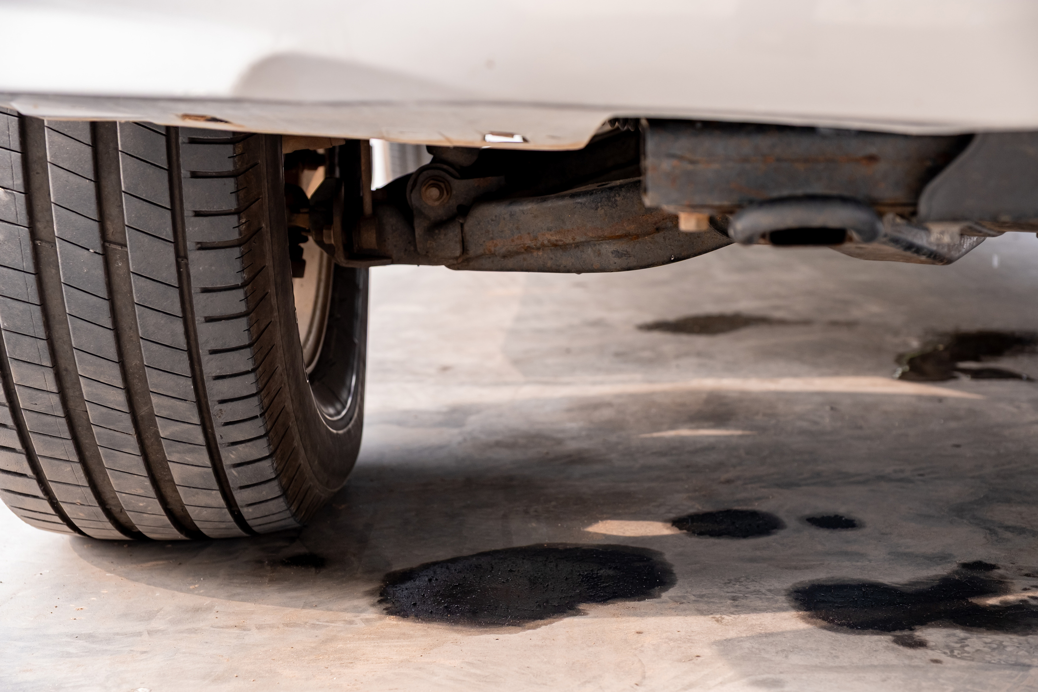 Oil leaking from underneath a car pools on a concrete floor