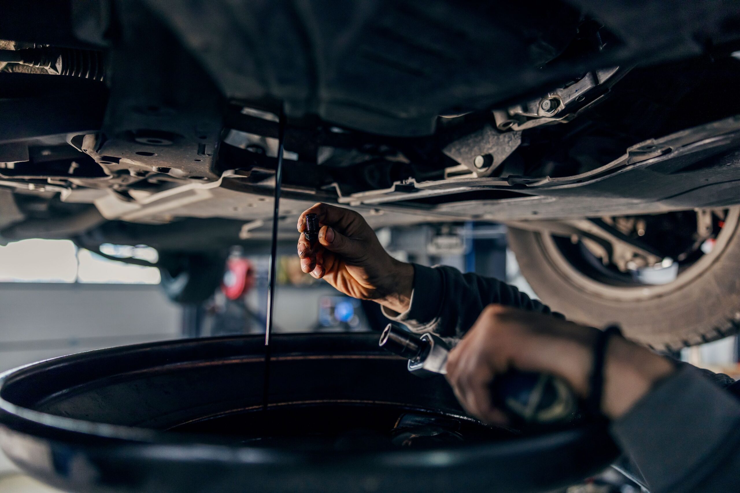 A technician drains a car's oil tank from beneath